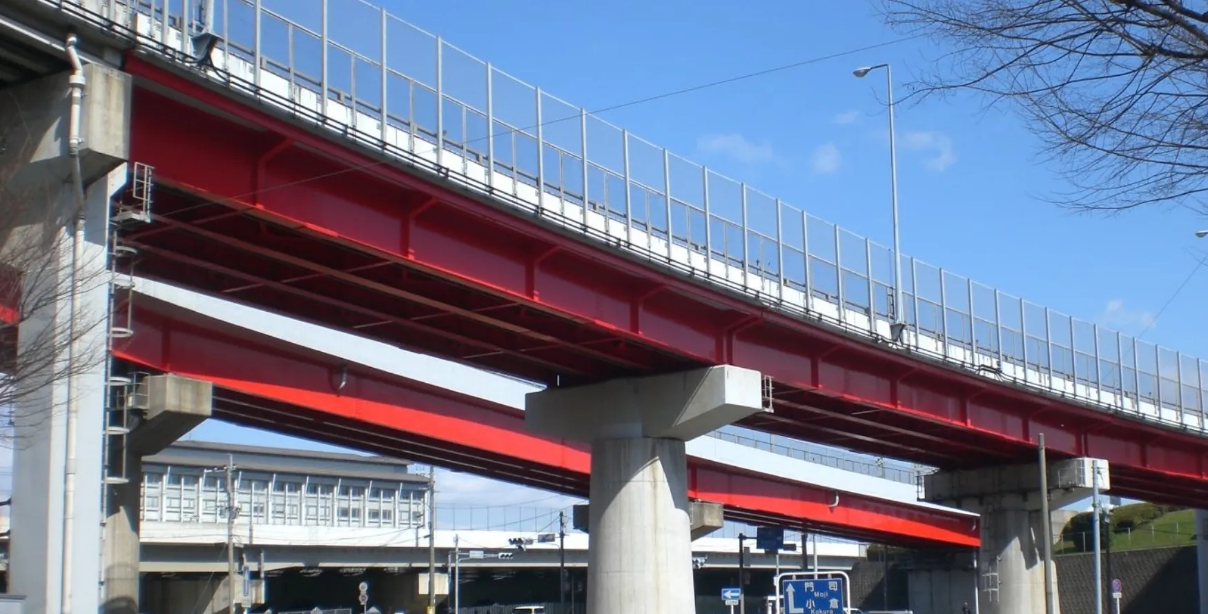 青空を背景に、鮮やかな赤色で塗装された大規模な高架道路の橋梁。インフラ維持に貢献する橋梁塗装・防食の施工事例