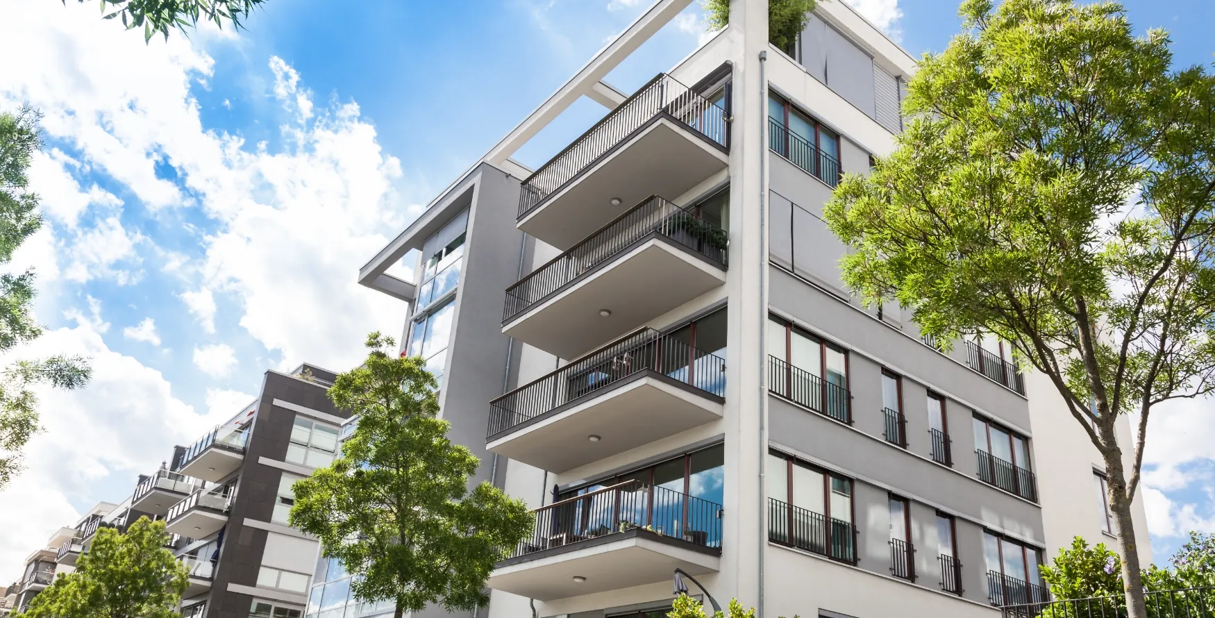 白とグレーを基調としたモダンなマンションの外観と、手入れされた街路樹。住宅設備の長寿命化を実現する防食技術の活用例