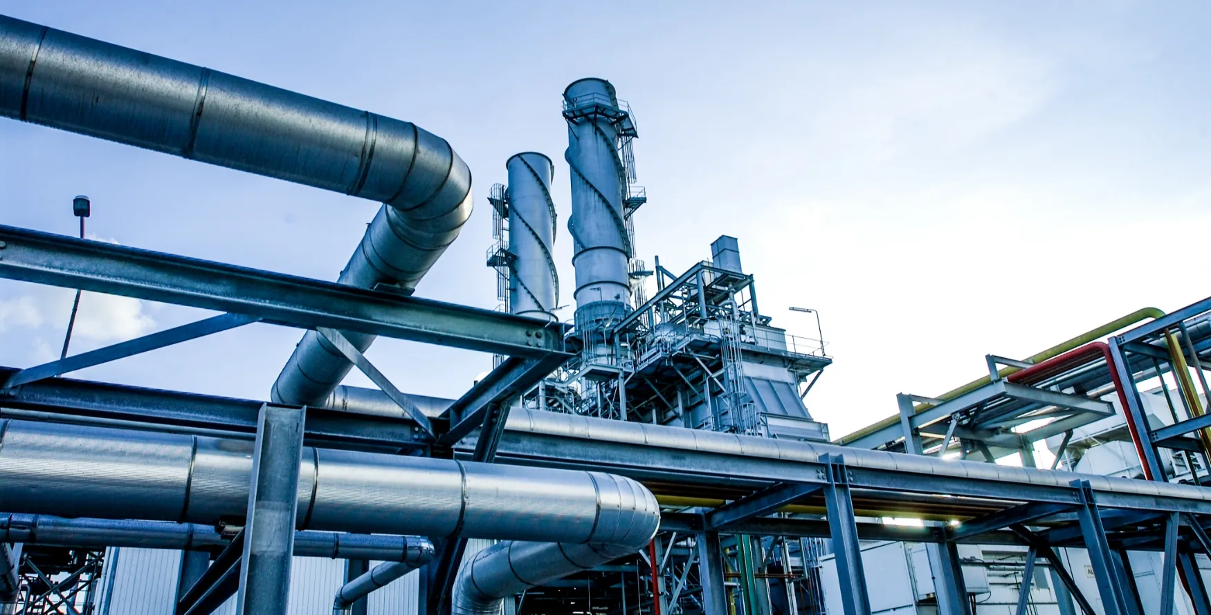 下から見上げるようなアングルで捉えた、巨大な産業プラントの銀色のパイプラインと蒸留塔の迫力ある風景