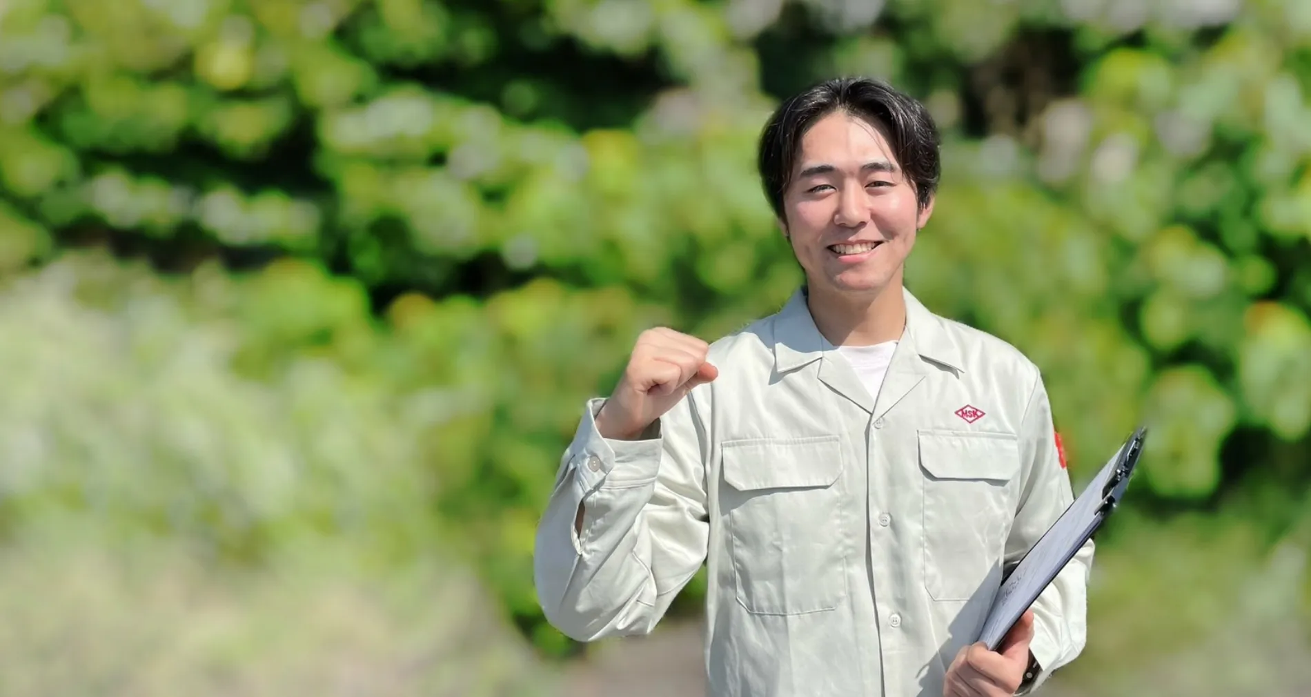 笑顔でガッツポーズをする、グレーの作業服を着た若い男性社員。