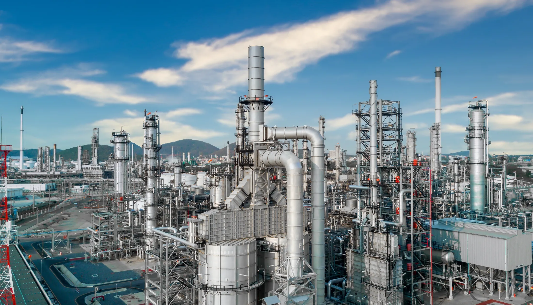 青空の下に広がる、複雑な配管と無数の蒸留塔が立ち並ぶ大規模な石油化学プラントの全景