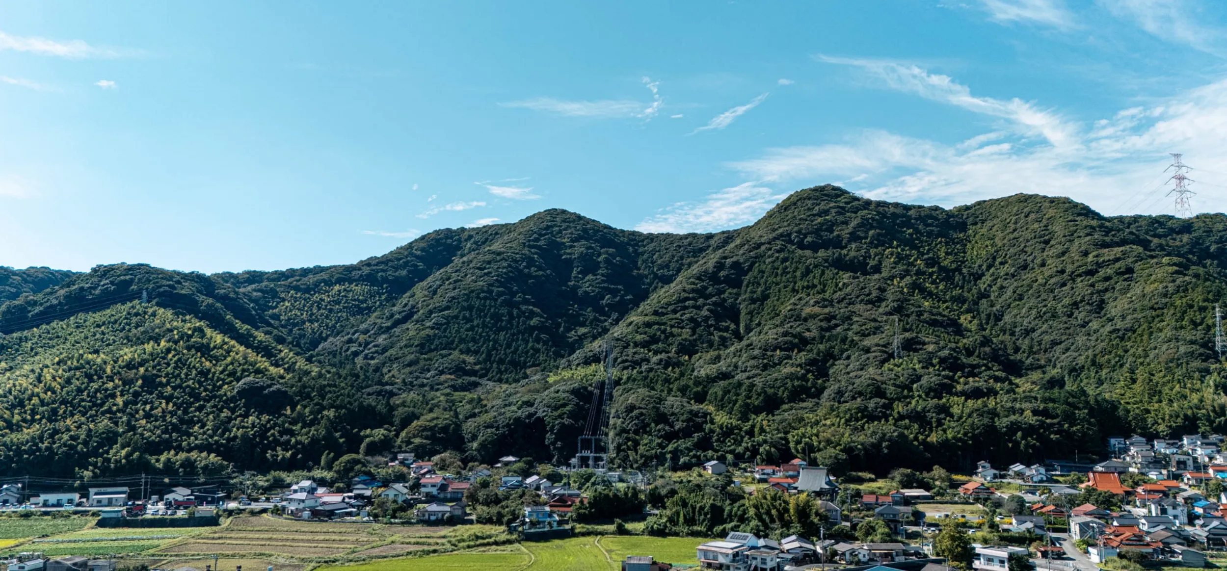 青空の下、緑豊かな山々に囲まれたのどかな日本の集落の風景。