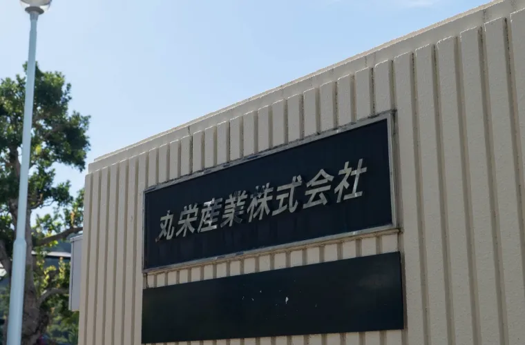 建物の入り口付近にある、黒い背景に白い文字で「丸栄産業株式会社」と書かれた社名板。